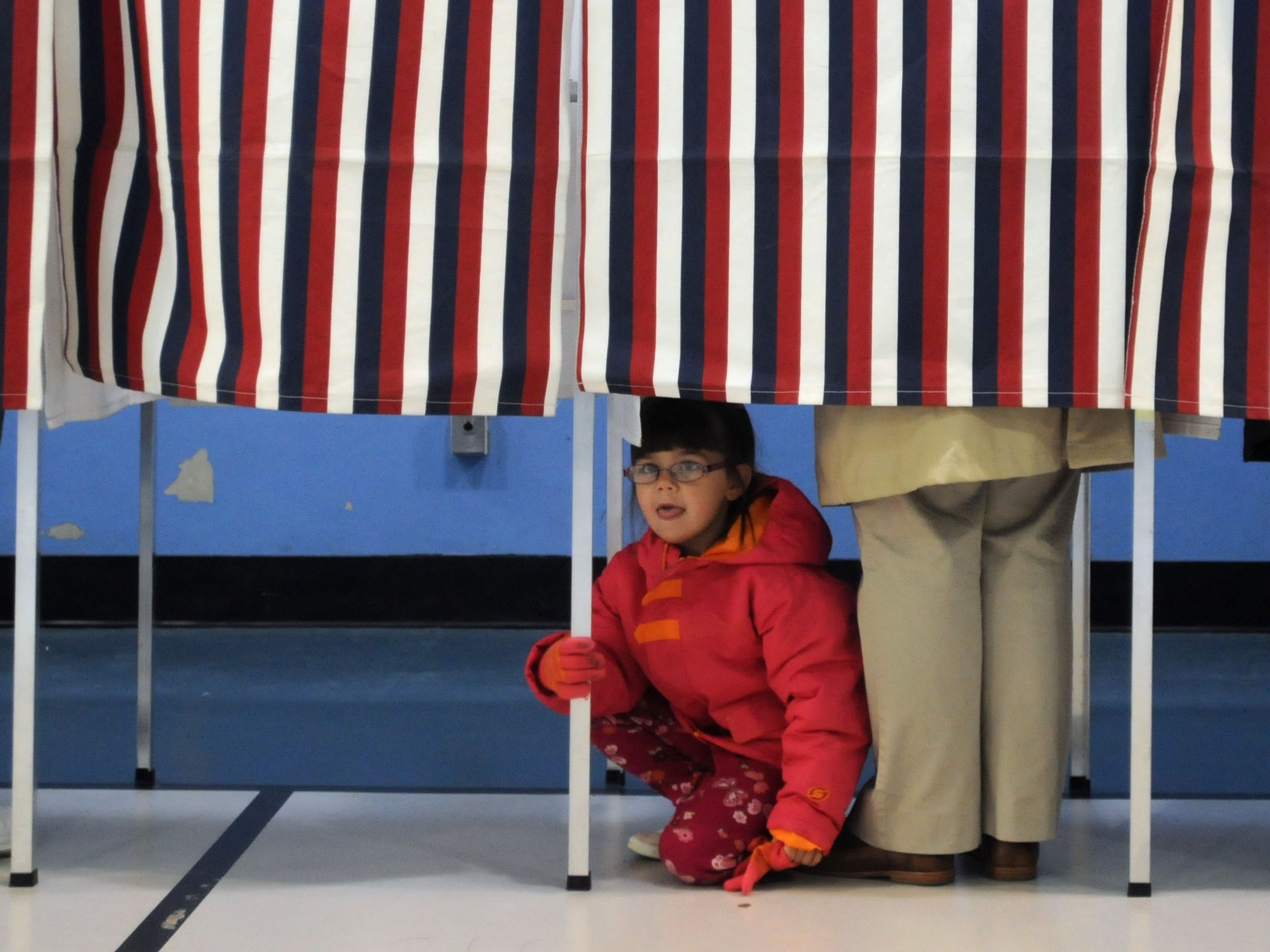 A young girl looks out from a voting booth as her mother casts her ballot at the Bishop Leo O'Neil Youth Center on November 6, 2012 in Manchester, New Hampshire. The swing state of New Hampshire is recognised to be a hotly contested battleground that offers 4 electoral votes, as recent polls predict that the race between U.S. President Barack Obama and Republican presidential candidate Mitt Romney remains tight. (Photo by Darren McCollester/Getty Images)