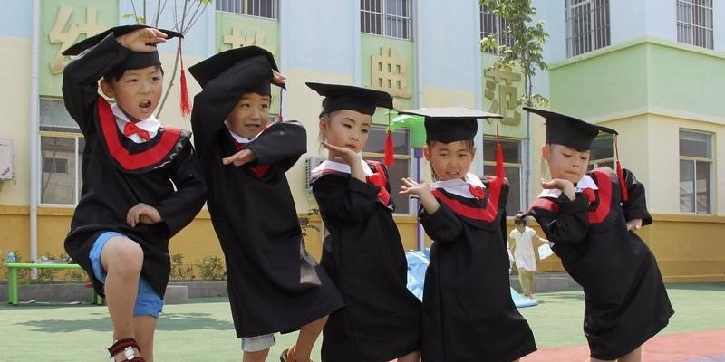 Children in gowns and mortarboards pose for pictures during their kindergarten graduation ceremony, in Wenxian county, Henan province July 2, 2014.  REUTERS/Stringer